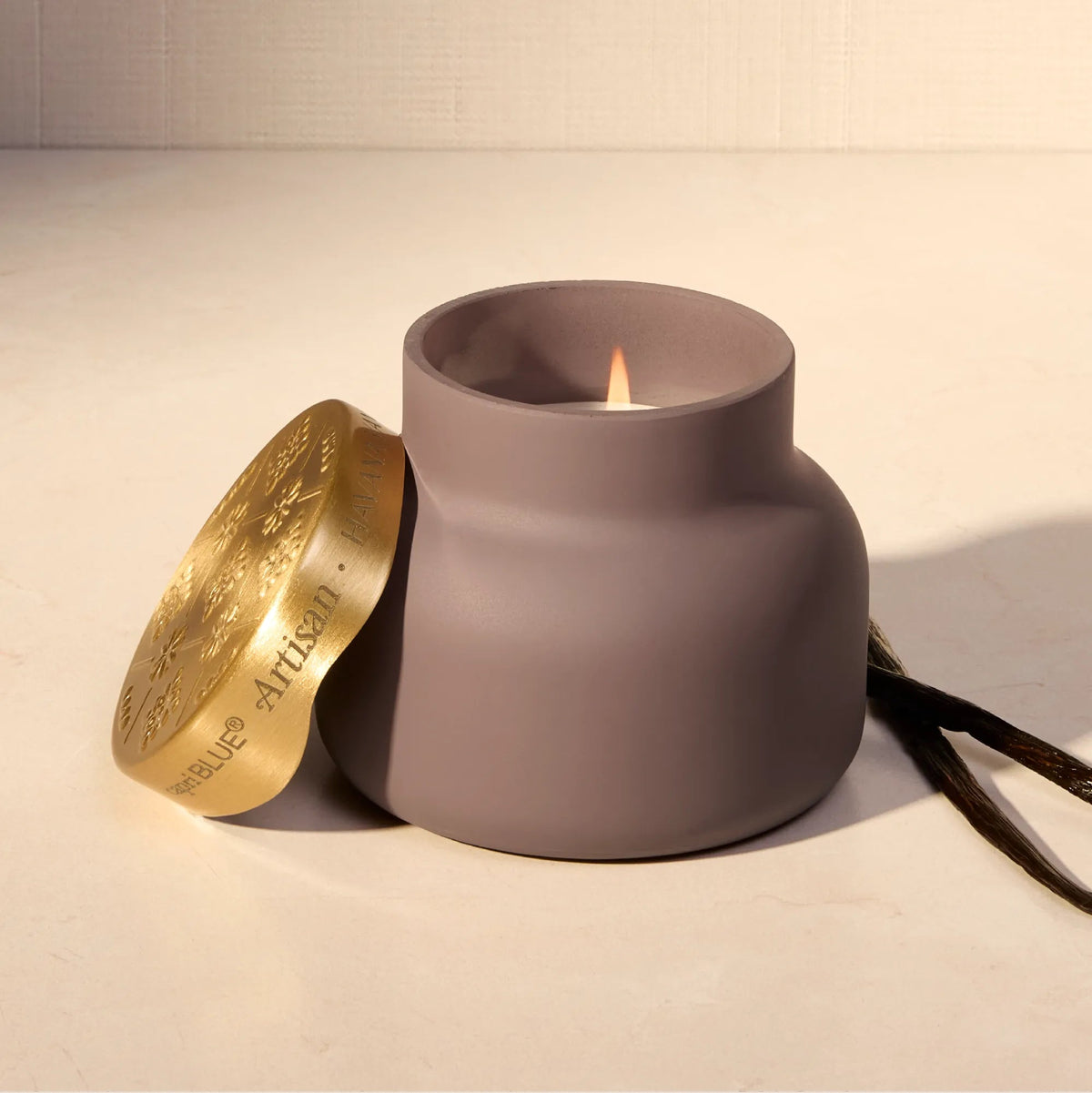 Lit Capri Blue Havana Vanilla Terrazza Velluto Candle in a matte purple vessel with an embossed gold lid & vanilla pods.
