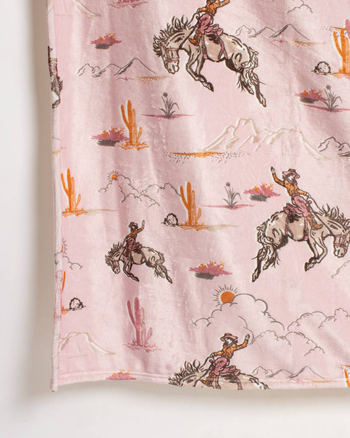 Pink Howdy Hunny Throw from The Royal Standard with a Western desert pattern of cowboys on broncos, cactuses, and mountains.