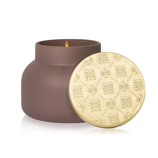 Capri Blue Havana Vanilla Terrazza Velluto Candle in a matte brown jar with a gold embossed lid, next to a lit flame.