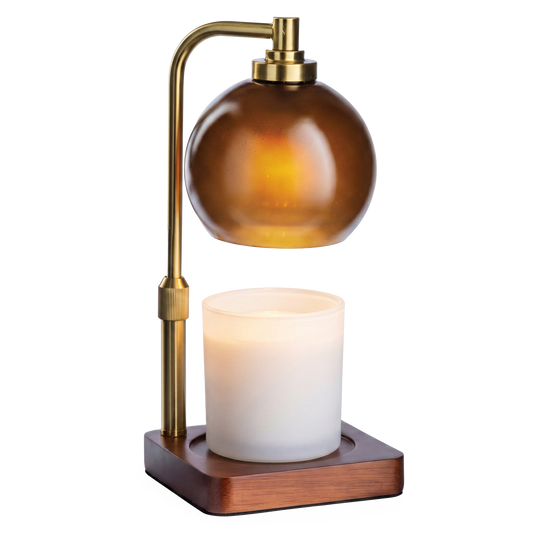 Amber Sphere Lamp by Candle Warmers Etc. with a brass arm and wooden base, warming a white candle.